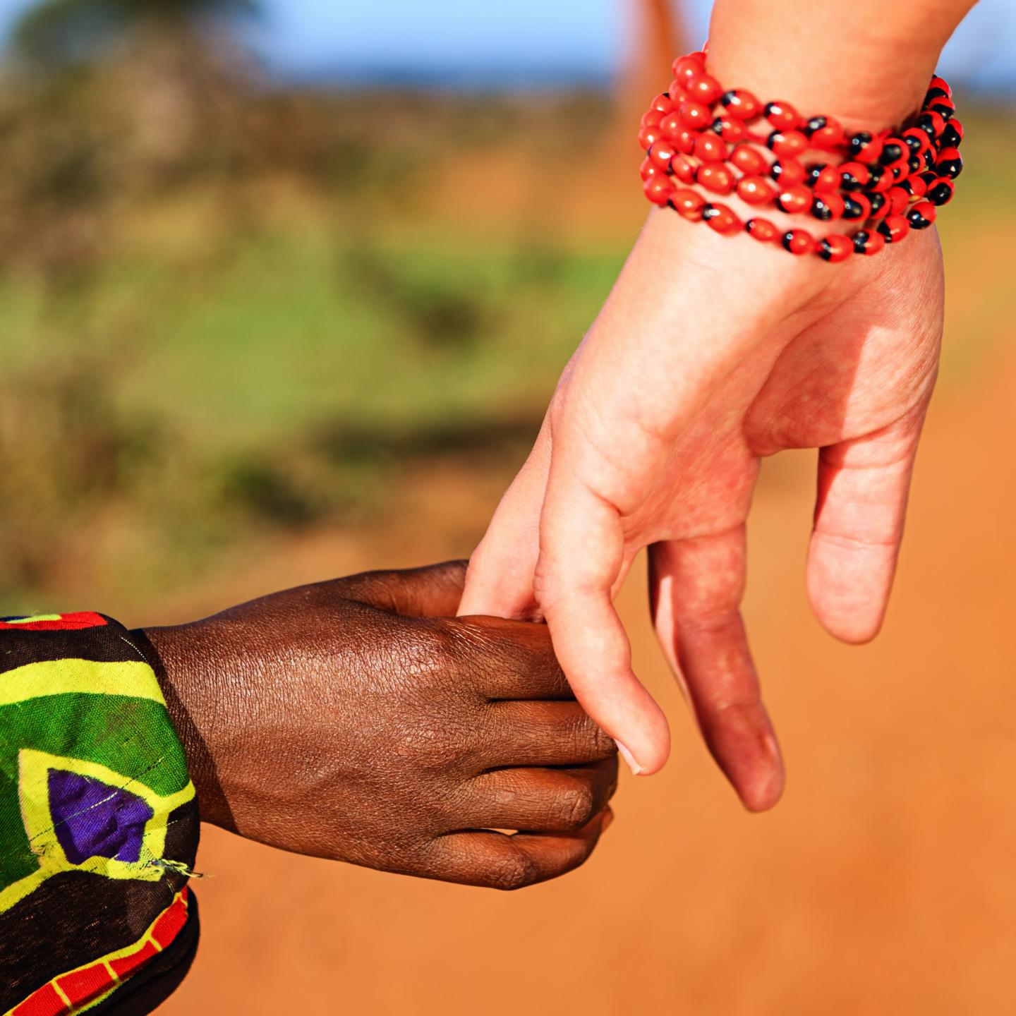 Nahaufnahme. Afrika. Eine Frau mit Armband am Handgelenk hält die Hand eines Kindes in afrikanischer Kleidung.