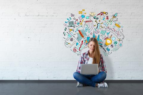 Eine junge Frau sitzt mit einem Laptop auf dem Boden. Auf der Wand hinter ihr illustrierte Symbole für Digitales.