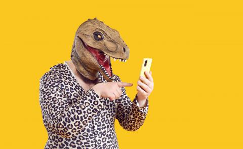 Person hat Dino-Maske auf und ein Smartphone in der Hand