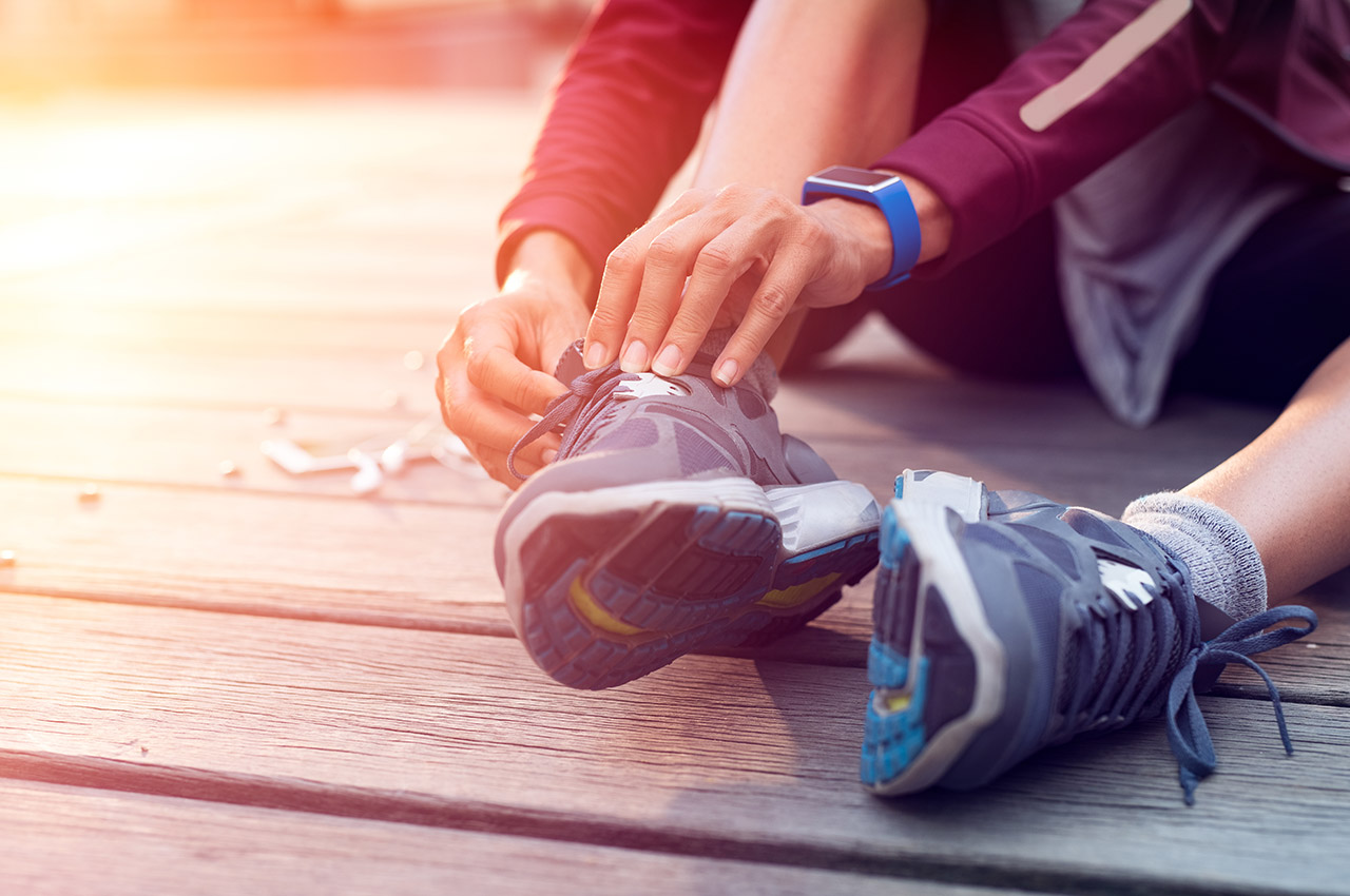 Closeup hand of runner tying laces of her sport shoes. Woman sitting on floor and lacing training sneakers before getting ready for workout. Hands of sportswoman tying shoelaces on sporty sneaker.