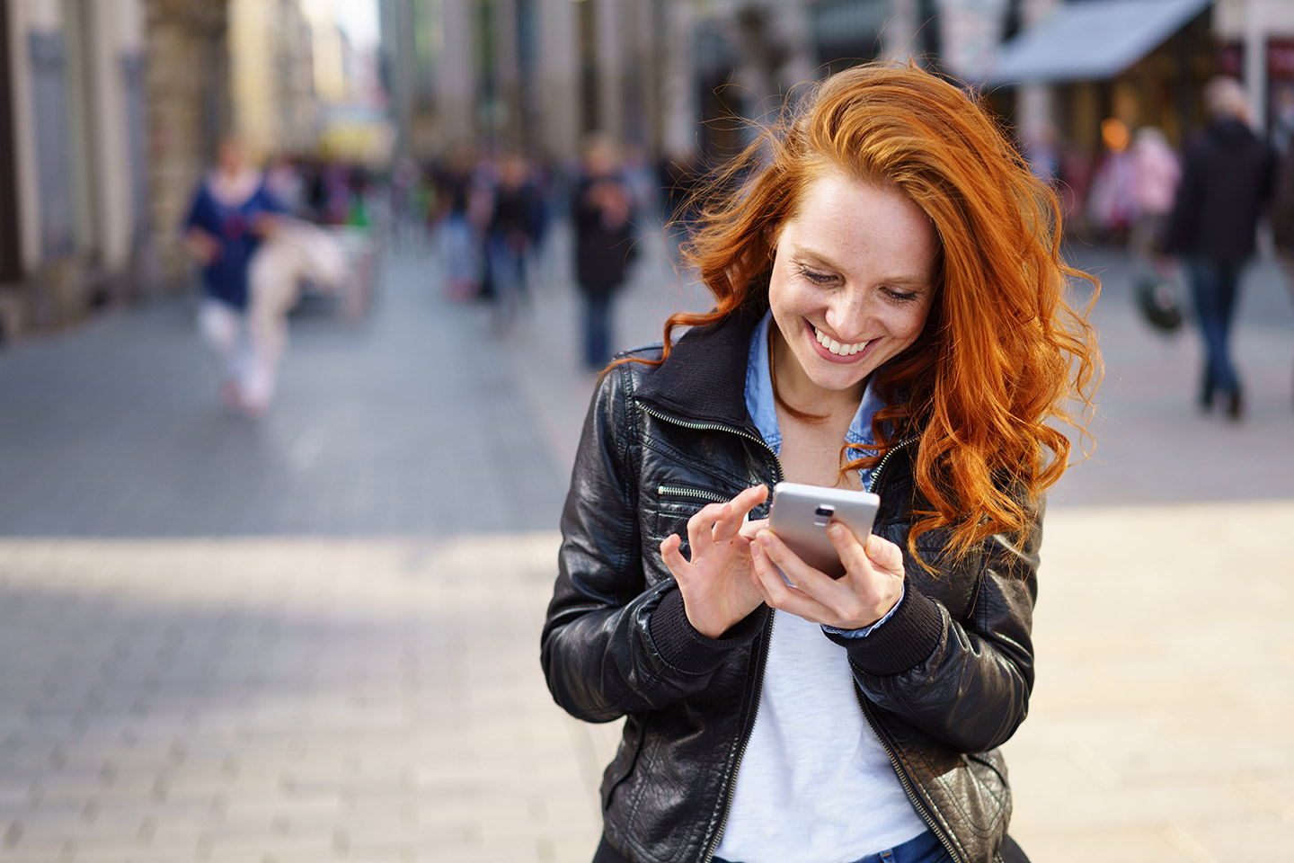 glückliche frau steht in der stadt und tippt auf ihrem handy