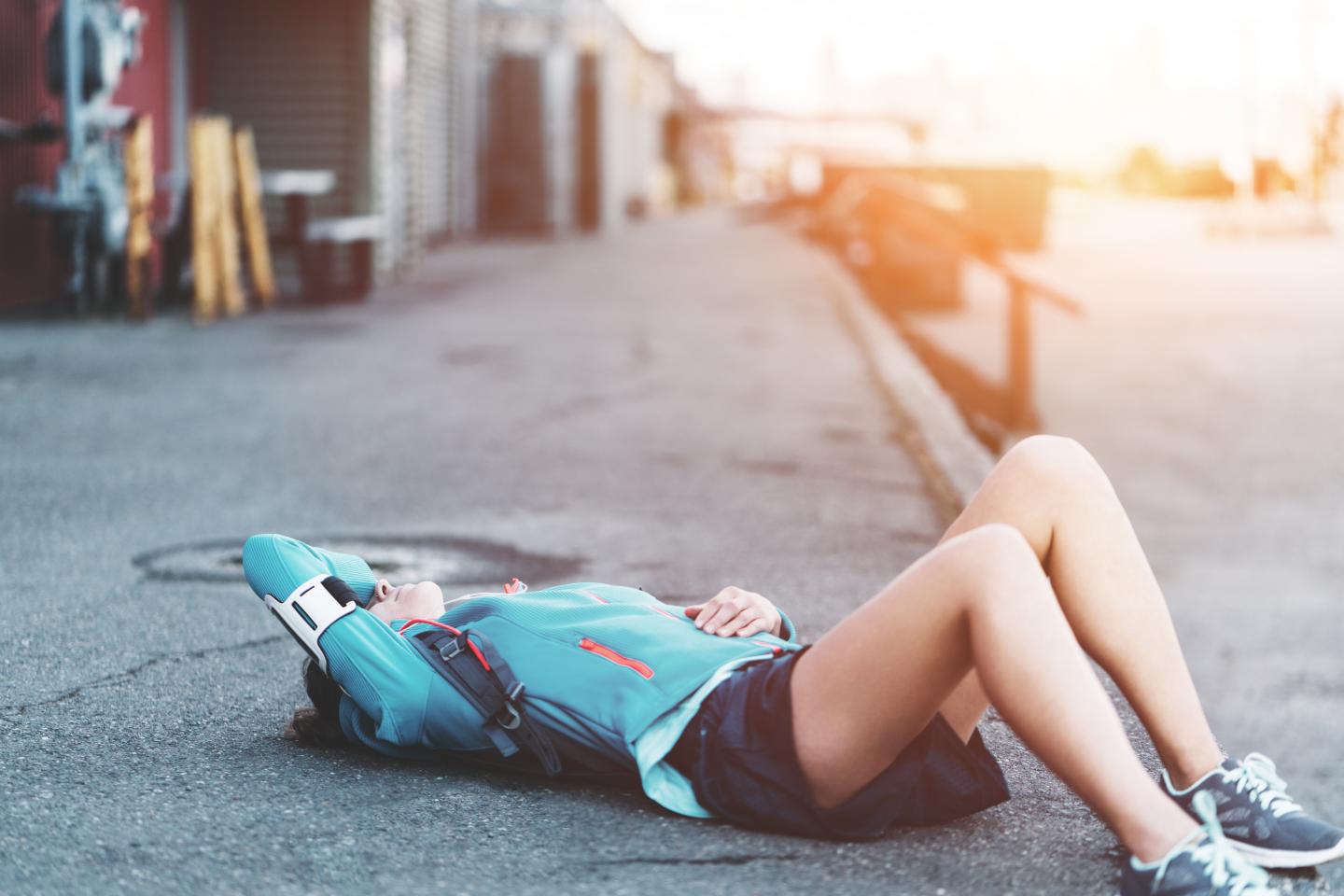 Eine junge Frau in Sportkleidung liegt ausgepowert auf dem Gehweg.