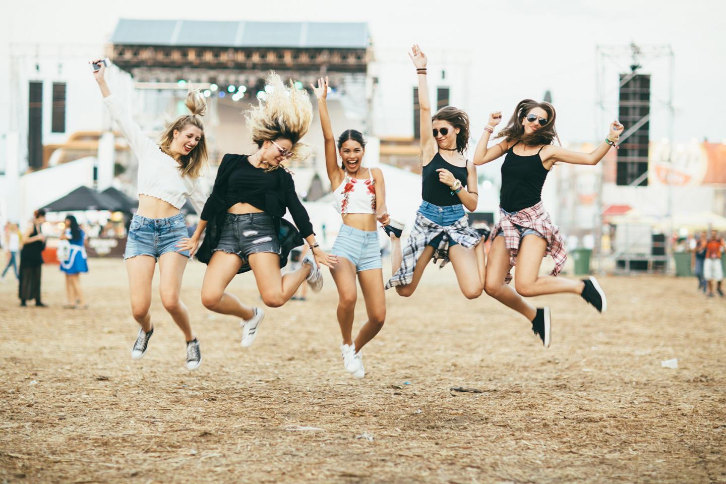 Eine Gruppe junger Frauen auf einem Festival springt energiegeladen in die Höhe.