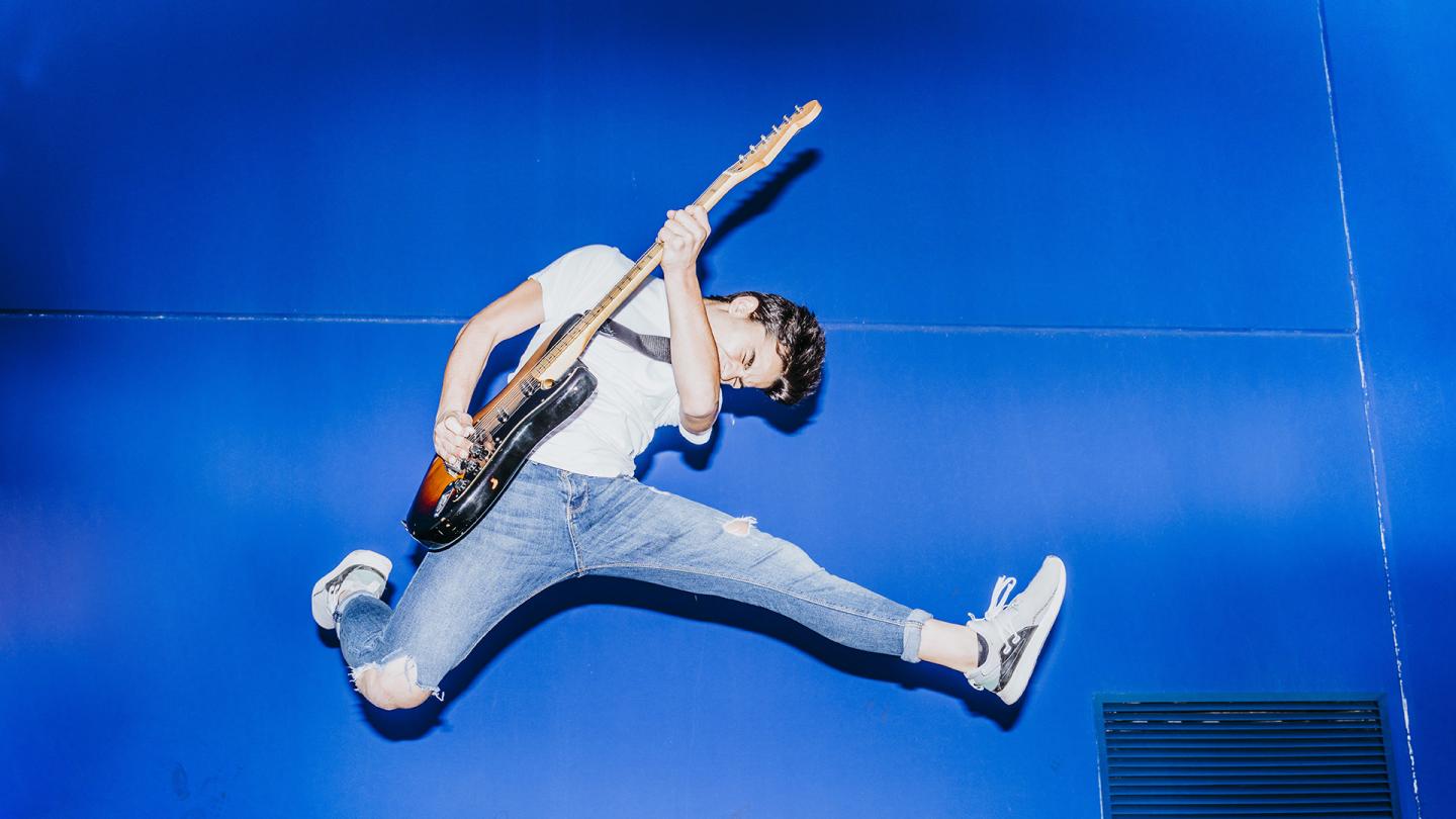 Ein junger Mann mit Gitarre springt in die Luft.