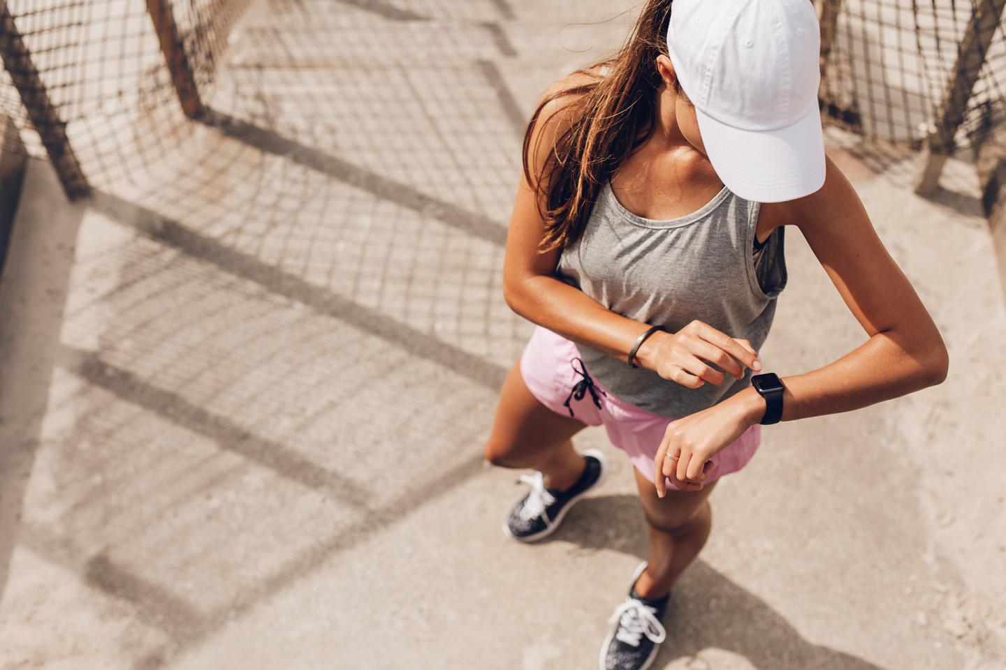 Junge Frau in Sportkleidung blickt auf ihre Smartwatch.