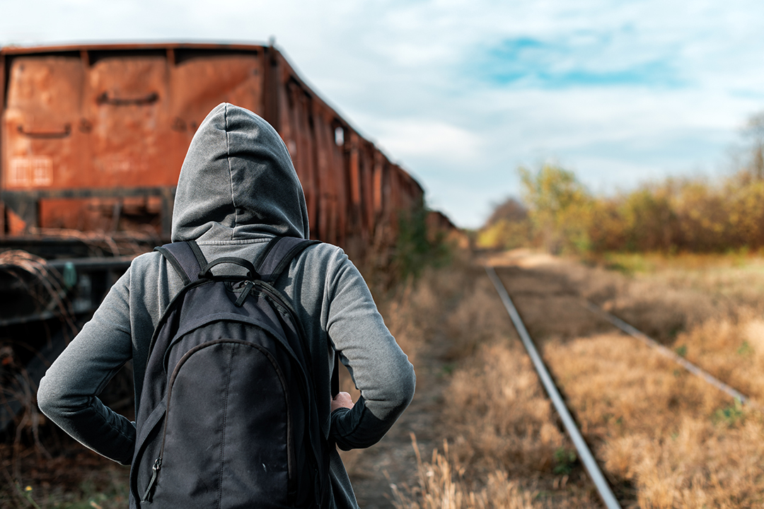 Eine junge Frau in Kapuzenpullover läuft vor der Kamera weg auf verlassenen Zugschienen neben alten Wagons.