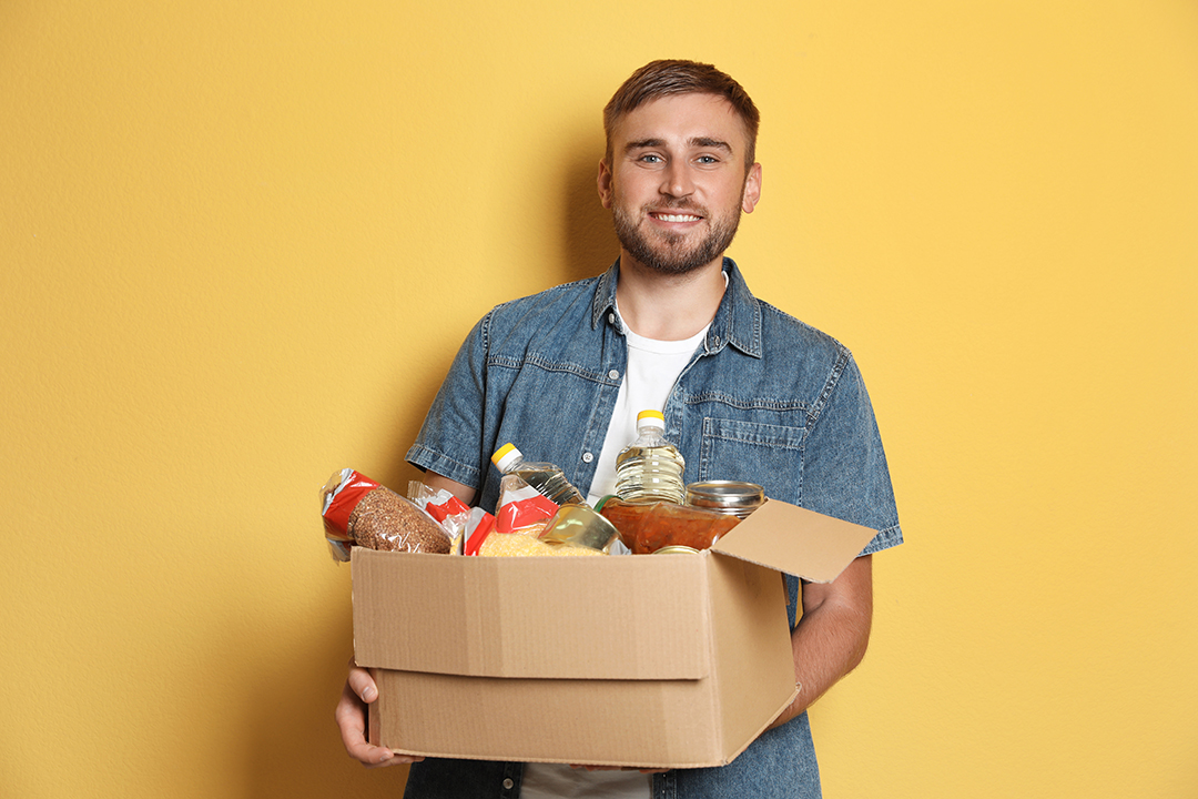 Ein junger Mann hält einen Karton voller Nahrungsmittel.
