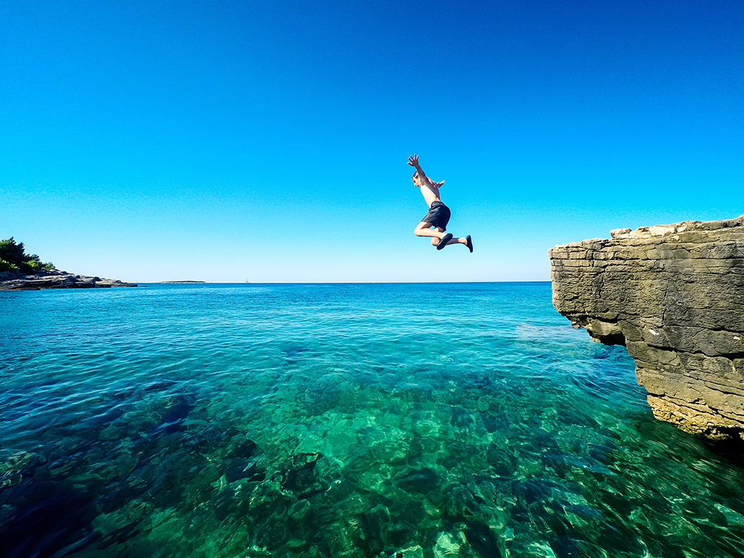Ein Mann springt von einer Klippe ins offene Meer