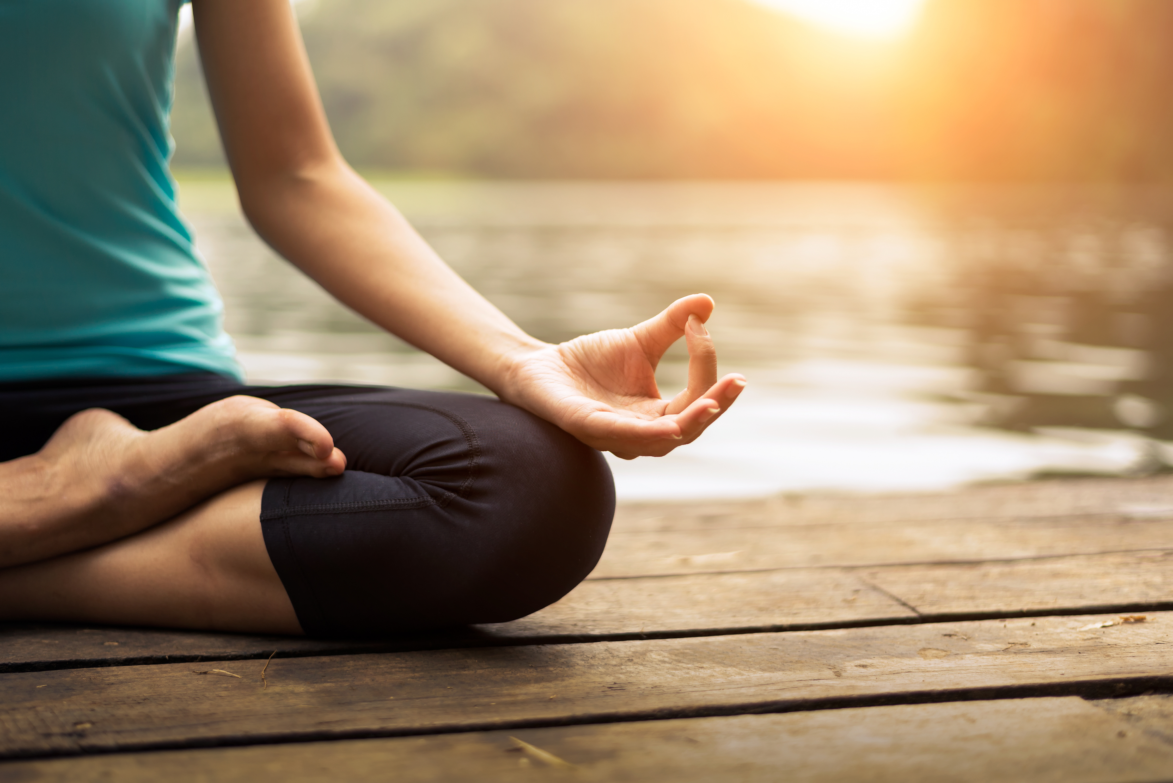 Eine junge Frau sitzt im Lotus-Sitz an einem See.