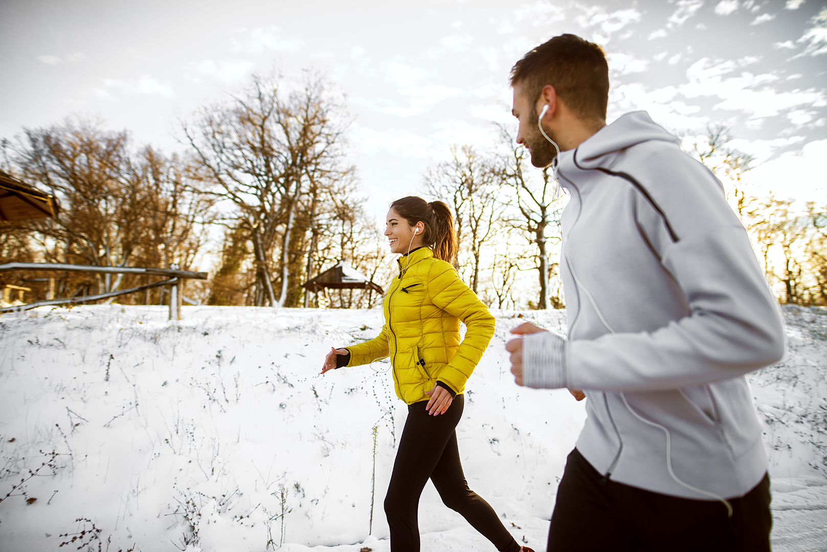Ein Paar joggt in verschneiter Landschaft. Beide lachen.