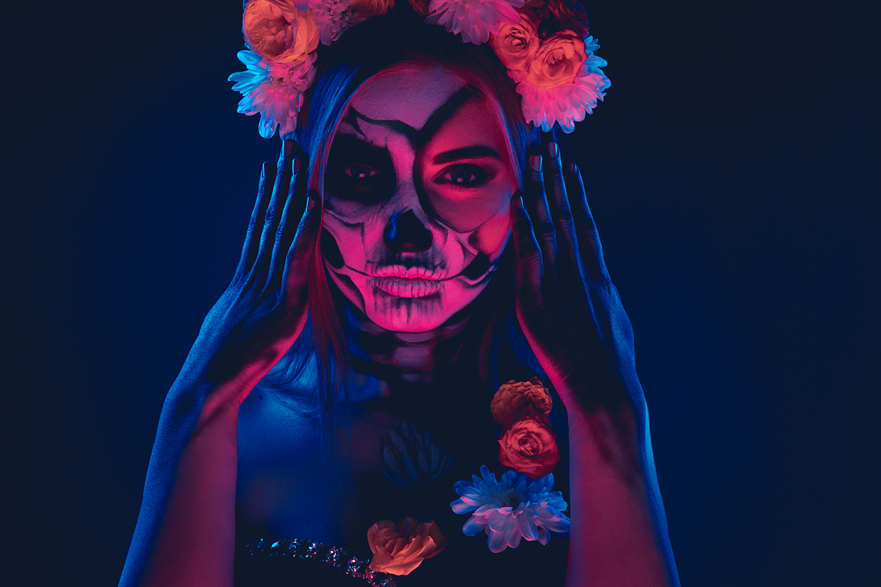 Eine junge Frau mit Totenkopf-Make-up blickt in die Kamera. Ihr Kostüm ist angelehnt an die typische Tracht des mexikanischen Feiertags Día de los Muertos