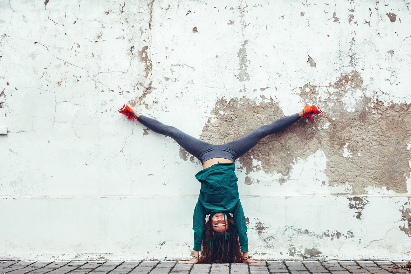 Eine junge Frau macht vor einer Wand einen Handstand.