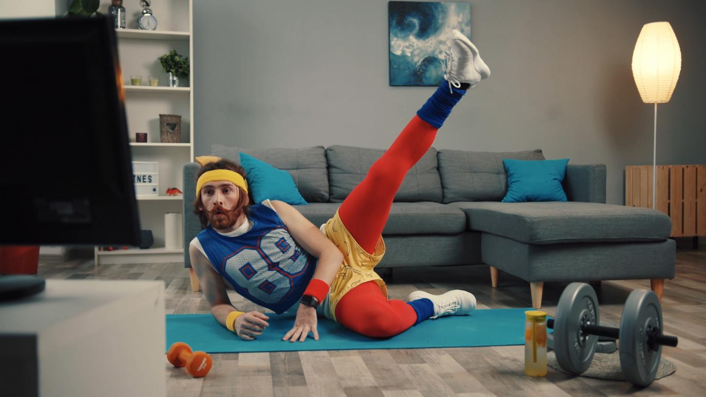 Ein in lustiger Sportkleidung gekleideter Mann macht Gymnastik vor dem Fernseher.