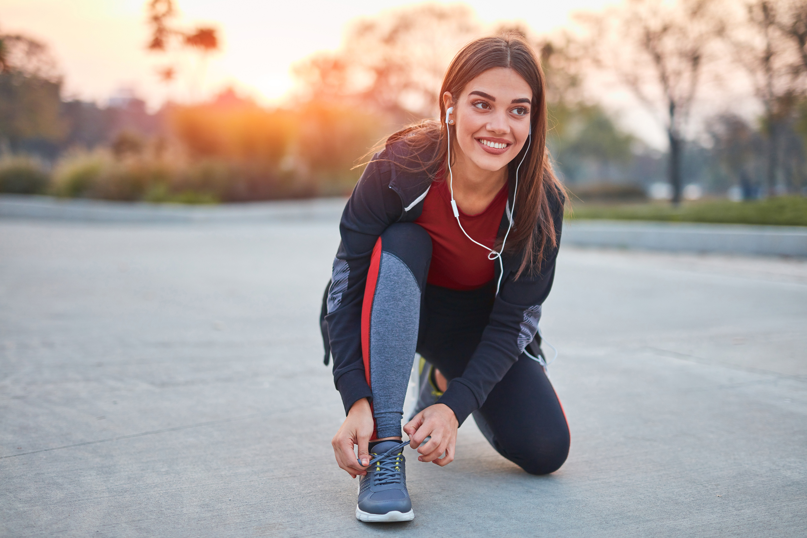 Eine strahlende junge Frau schnürt ihre Sneaker. Sie trägt Sportkleidung und macht sich bereit für ihren Lauf
