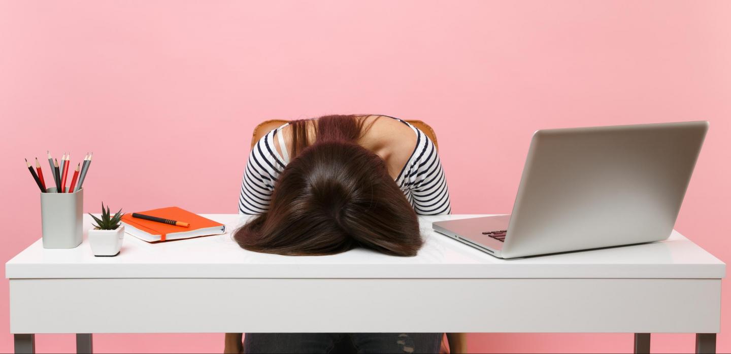 Junge Frau sitzt gestresst an Schreibtisch und hat Kopf auf Tischplatte gelegt
