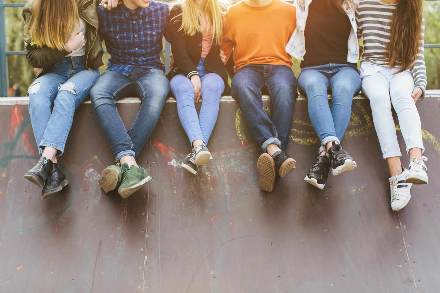 junge Menschen sitzen nebeneinander auf einer Mauer, man sieht nur ihre Beine