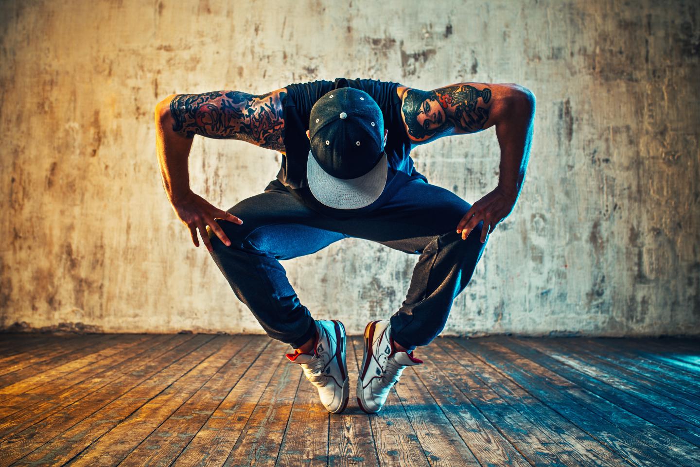 Mann mit Tattoos steht in Tanzpose vor bunter Wand