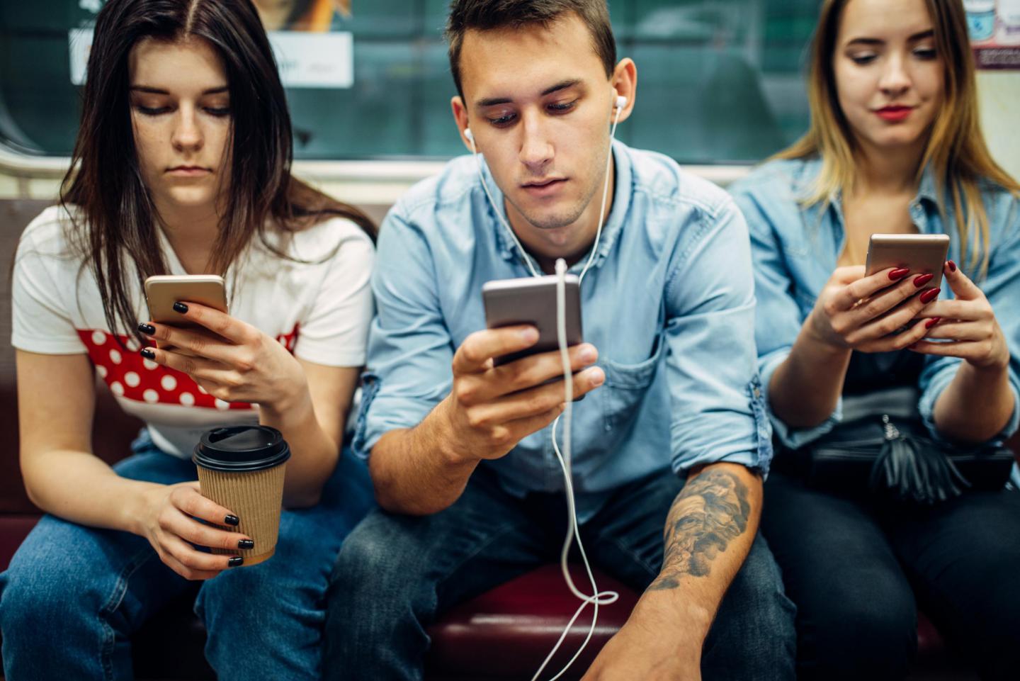 junge Leute sitzen in der Bahn und gucken auf ihre Handys