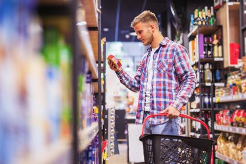 Junger Mann schaut sich im Supermarkt die Zutatenliste eines Produkts an