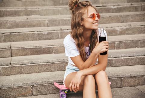 Junge Frau sitzt auf Treppenstufen und trinkt eine Cola