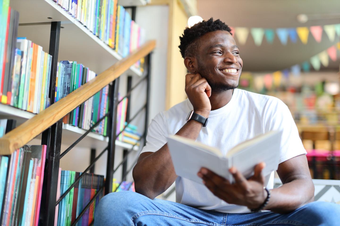 Junger Mann mit Buch in der Hand sitzt auf Treppe in Bibliothek