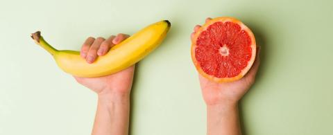 Sex ed and sexual health. Young person holding a banana and grapefruit against a green background
